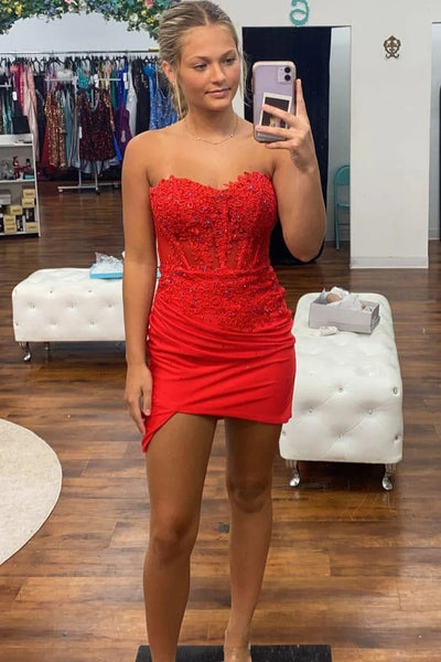A woman takes a mirror selfie in a boutique wearing a bright red strapless sweetheart mini dress with a beaded bodice and ruched skirt. 