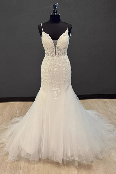 An ivory white lace and tulle wedding gown displayed on a black dress form mannequin against a dark gray wall and light wood floor.
