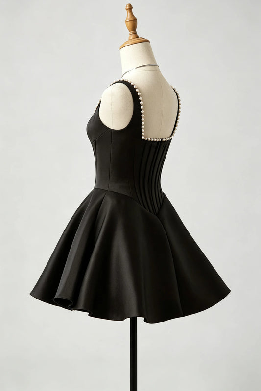 A black sleeveless fit-and-flare homecoming dress displayed on a cream dress form mannequin, showing the back view with a pearl-trimmed neckline and pleated corset-style back panel, against a light gray studio background.