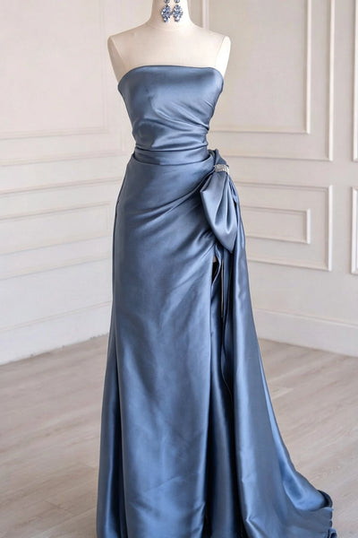 A strapless floor-length satin gown in a dusty slate blue color, displayed on a cream mannequin in an elegant indoor setting with white paneled walls and light wood flooring.
