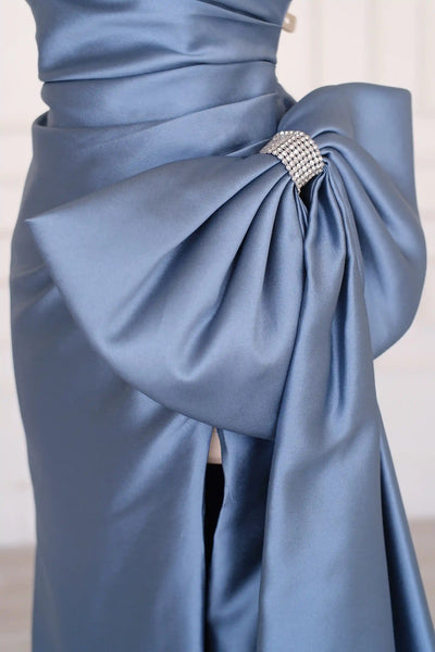 A strapless floor-length satin gown in a dusty slate blue color, displayed on a cream mannequin in an elegant indoor setting with white paneled walls and light wood flooring.