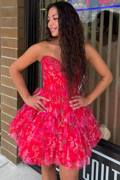 A woman wearing a fuchsia strapless tulle dress with a floral pattern and beaded sweetheart neckline, posing in front of a storefront window.