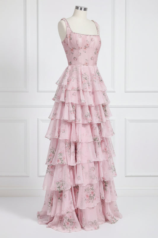 A pink tiered maxi dress with a floral print, displayed on a mannequin against a white paneled wall.
