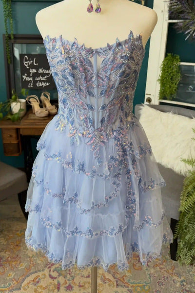 A ice blue strapless tulle dress with floral lace applique and a corset-style bodice, displayed on a mannequin in an indoor room setting.