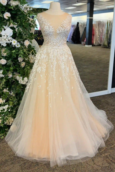 A sleeveless A-line ball gown with a deep V-neckline, heavily embellished with white floral lace and beadwork on a peach-colored tulle skirt, displayed on a mannequin in a bridal boutique.