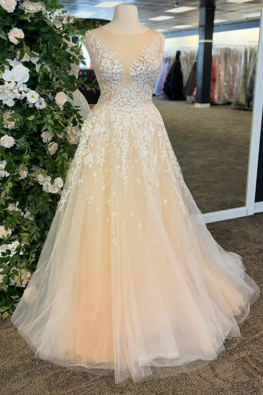 A sleeveless A-line ball gown with a deep V-neckline, heavily embellished with white floral lace and beadwork on a peach-colored tulle skirt, displayed on a mannequin in a bridal boutique.