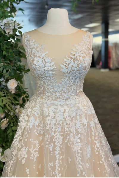 A sleeveless A-line ball gown with a deep V-neckline, heavily embellished with white floral lace and beadwork on a peach-colored tulle skirt, displayed on a mannequin in a bridal boutique.