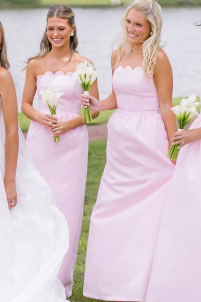 A bride in a white strapless gown stands with five bridesmaids wearing matching light pink strapless dresses, holding flower bouquets outdoors under a tree.