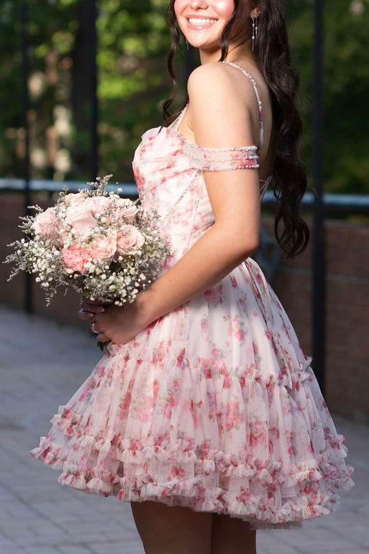 A woman wearing a short, off-the-shoulder pink floral tulle dress and holding a bouquet of pink roses and baby's breath outdoors.