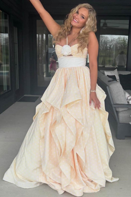 A woman wearing a strapless formal gown with a sweetheart neckline, a white floral bodice detail, a white waistband, and a voluminous layered skirt in a pale peach or cream tone, standing on a patio.