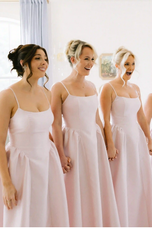 A sleeveless pink satin bridesmaid dress with a scoop neckline, displayed on a white mannequin in an indoor room with cream-colored walls and paneling.