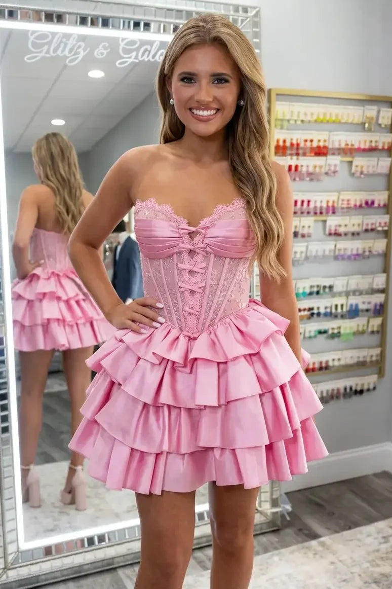A woman wearing a pink strapless corset homecoming dress with a ruffled tiered skirt.