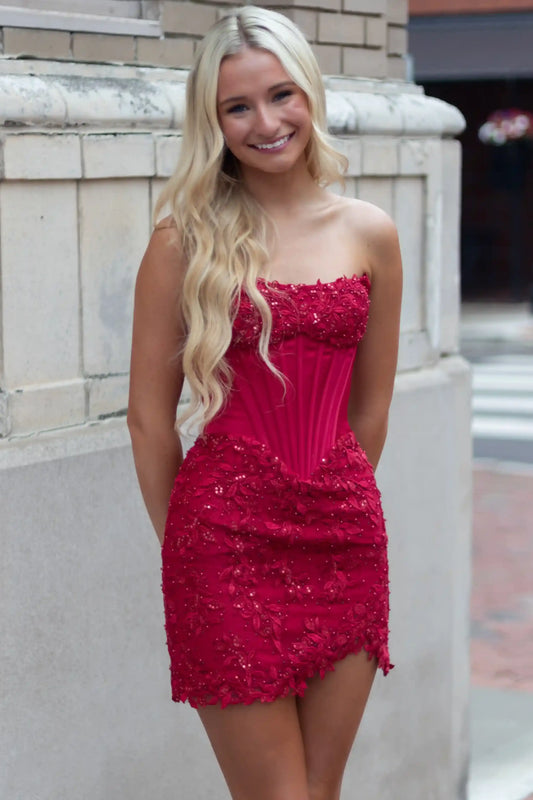 A smiling blonde woman wearing a bright red strapless mini dress with a corset-style bodice and beaded texture.