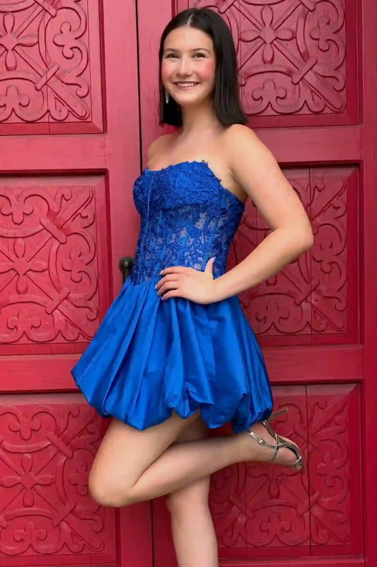 A young woman posing in a strapless royal blue applique and satin mini dress against a red decorative wooden door.