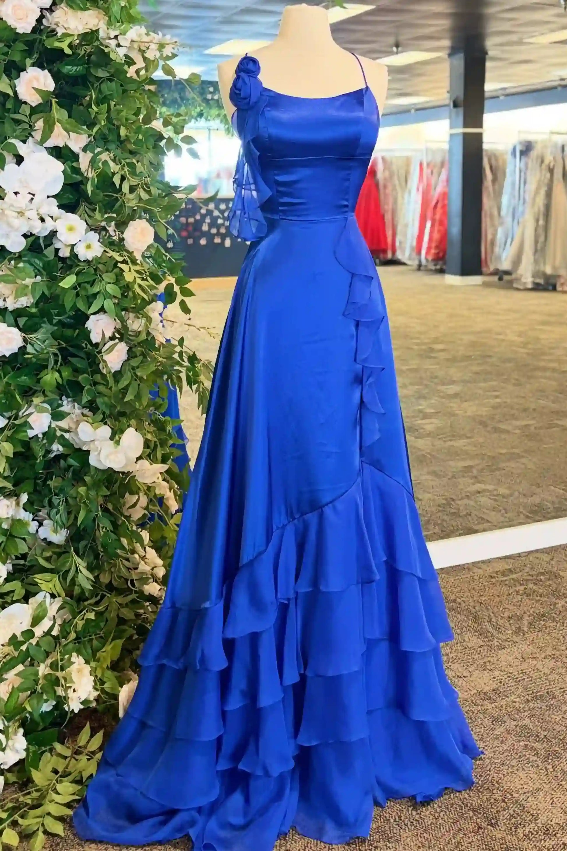 The dress features a fitted bodice, a single shoulder strap with a sheer draped detail, and a tiered ruffle skirt.