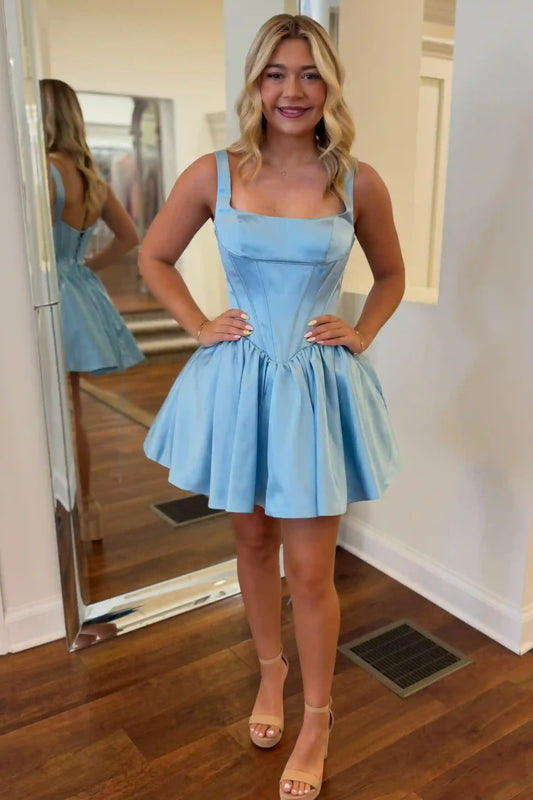 A woman modeling a light blue mini dress with a structured corset-style bodice and flared skirt, standing indoors with a mirror behind her showing the back of the dress.