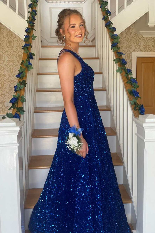 A woman wearing a sparkling royal blue sequined A-line dress stands on a decorated staircase, holding a small white and blue bouquet.