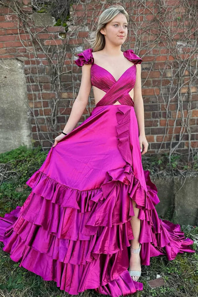A blonde woman wearing a shiny light pink formal gown with ruffled shoulder details, a sweetheart neckline, and a tiered ruffle skirt, standing outdoors in front of a glass building.
