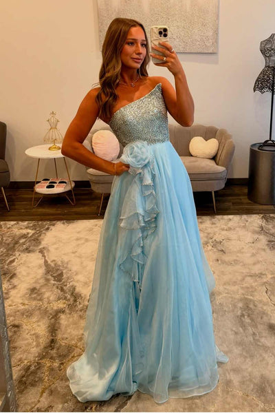 A woman takes a mirror selfie in a bright, light blue strapless formal gown with a sequined bodice and layered ruffle skirt, standing in a modern living room.