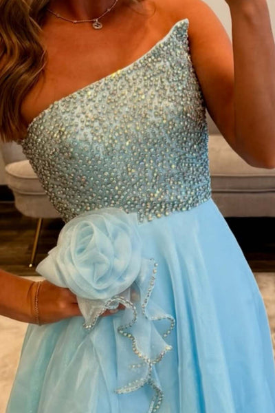 A woman takes a mirror selfie in a bright, light blue strapless formal gown with a sequined bodice and layered ruffle skirt, standing in a modern living room.