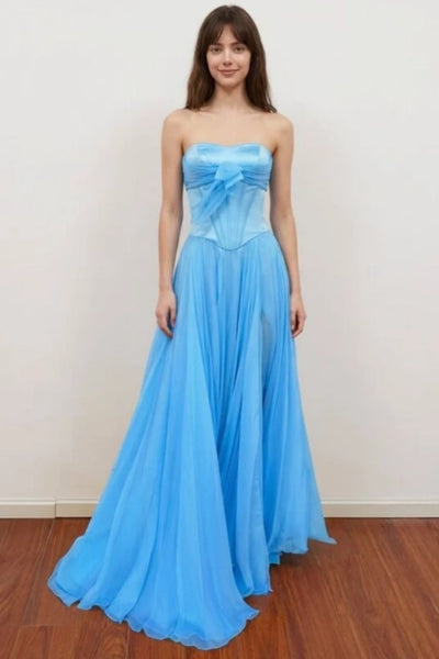 A woman models a strapless pink prom dress with a sweetheart neckline, a large bow detail at the waist, and a high thigh slit.