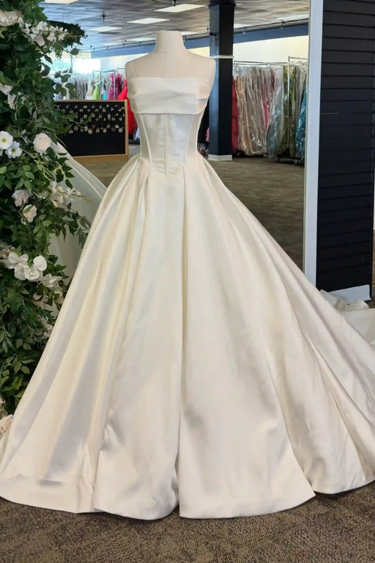 An ivory strapless ball gown displayed on a mannequin in a bridal boutique. The dress features a structured corset-style bodice and a full, flowing skirt that spreads across the floor.