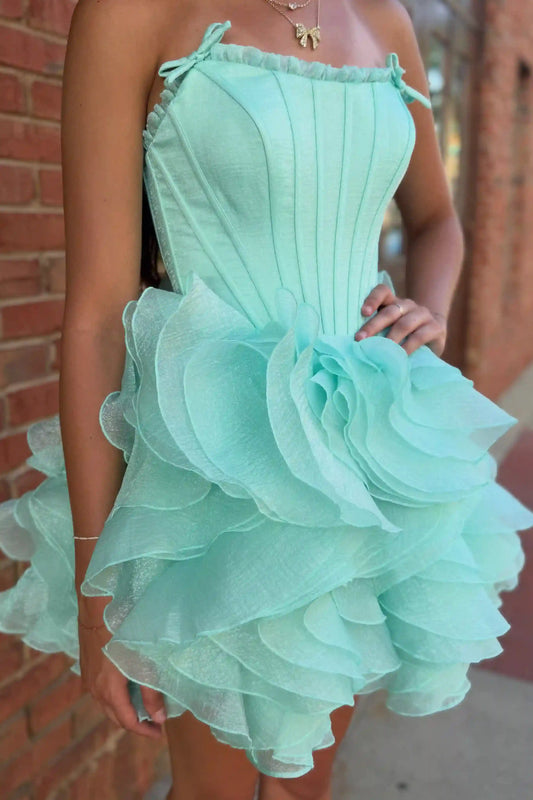 A mint green strapless mini dress with a structured corset-style bodice and a layered, ruffled tulle skirt, shown on a model standing in front of a brick wall.