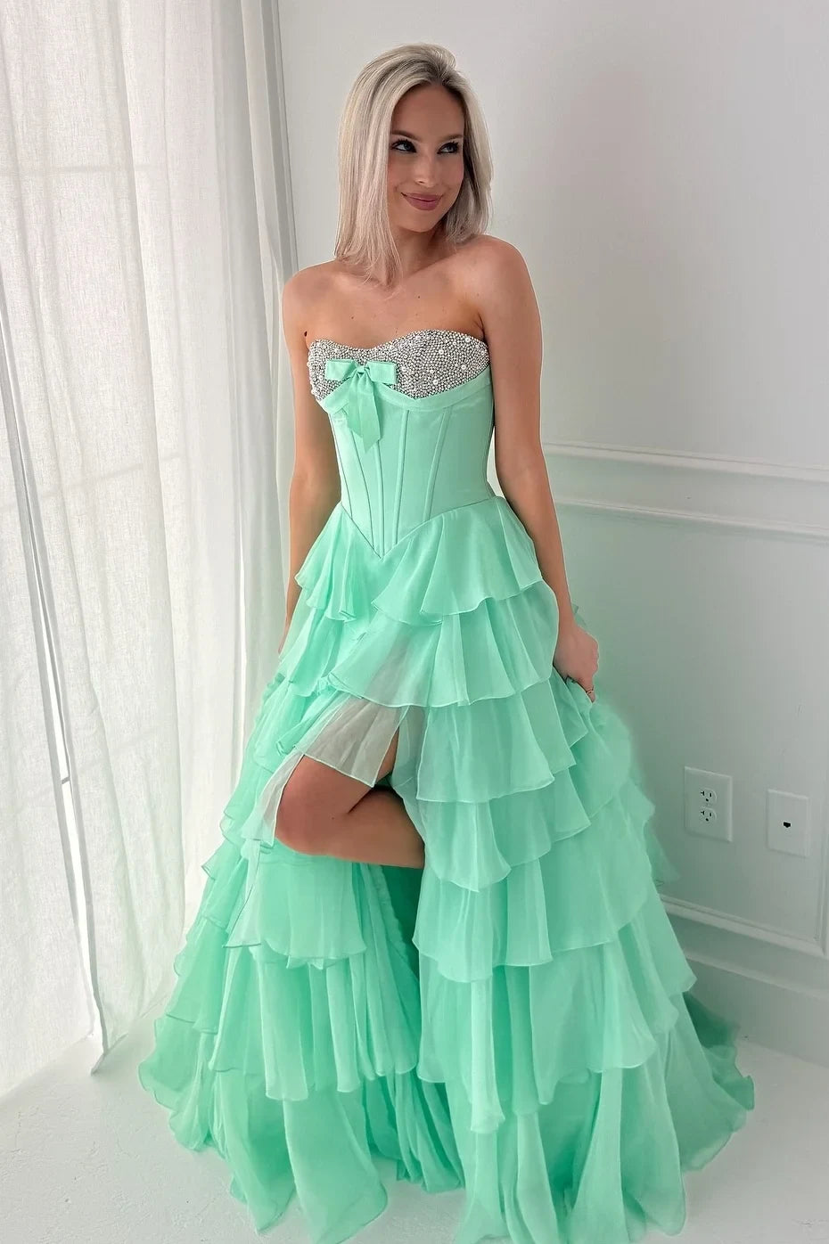 Woman wearing a mint green strapless dress with ruffled layers in a room.