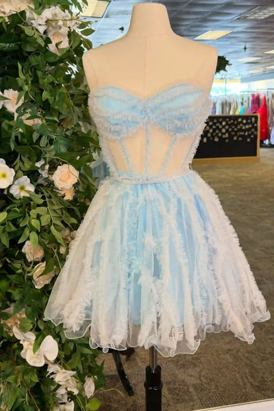 A light blue and white strapless tulle dress displayed on a mannequin torso in a retail setting, with a floral arrangement on the left and store fixtures in the background.