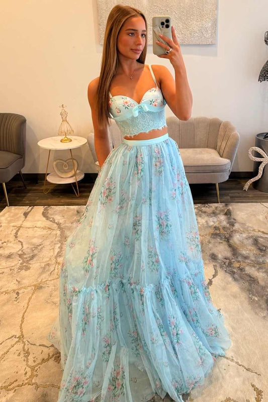A woman takes a mirror selfie wearing a light blue two-piece formal gown with a floral print. The dress features a sweetheart neckline crop top with lace applique and a matching tiered tulle skirt with pink and green floral details.