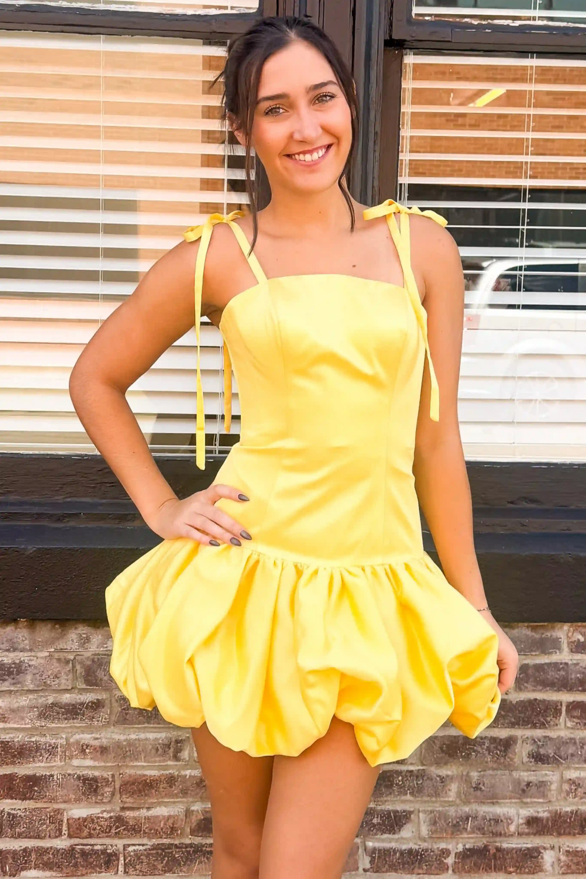 Young woman wearing yellow spaghetti strap bubble hem homecoming dress with bow
