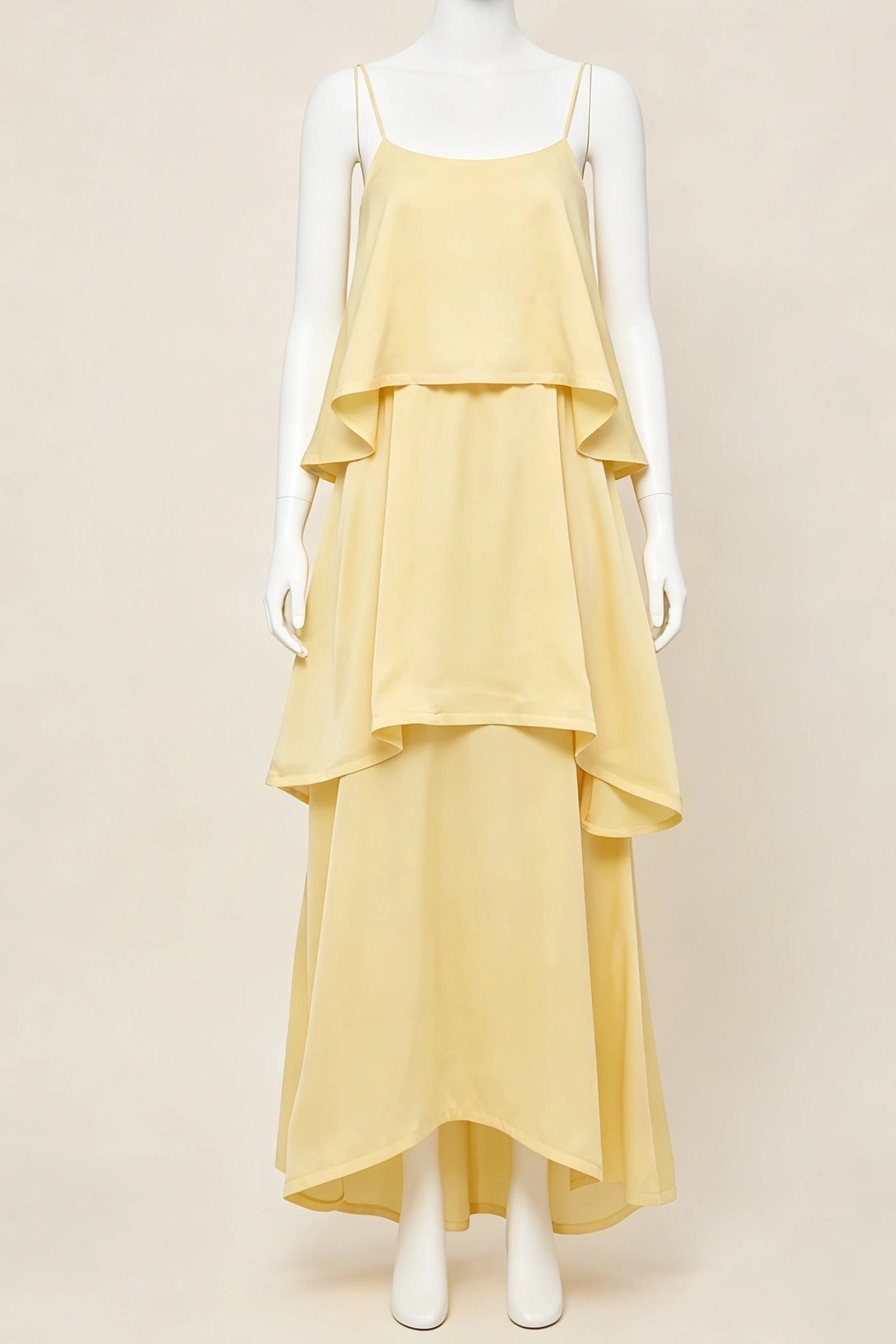 A pale yellow tiered maxi bridesmaid dress with spaghetti straps, displayed on a white mannequin against a solid beige background.