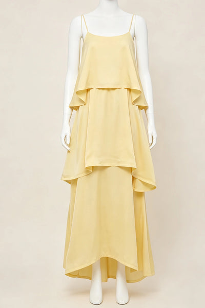 A pale yellow tiered maxi bridesmaid dress with spaghetti straps, displayed on a white mannequin against a solid beige background.