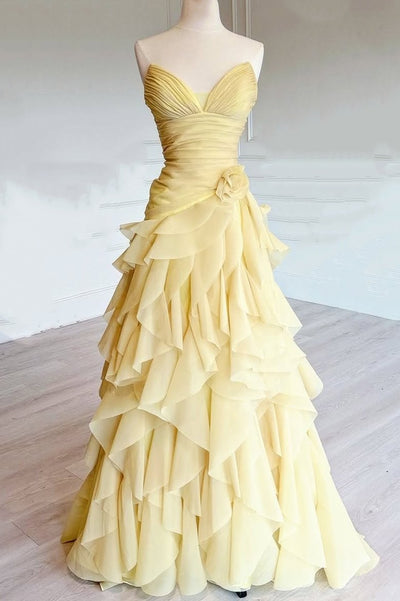 A yellow strapless ball gown with a sweetheart neckline, ruched bodice, and a dramatic tiered ruffle skirt, displayed on a mannequin in a bright indoor room.
