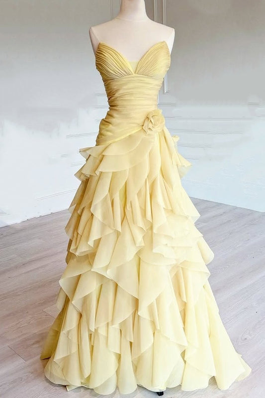 A yellow strapless ball gown with a sweetheart neckline, ruched bodice, and a dramatic tiered ruffle skirt, displayed on a mannequin in a bright indoor room.